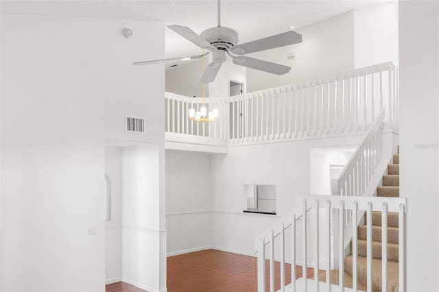 stairway with baseboards, visible vents, a ceiling fan, a towering ceiling, and wood finished floors