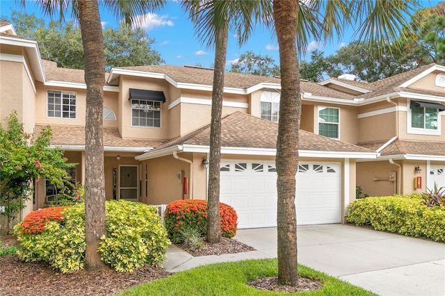 townhome / multi-family property with a garage, concrete driveway, a shingled roof, and stucco siding