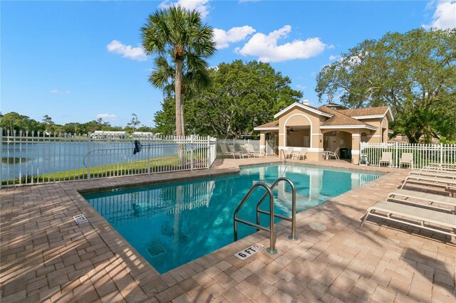 community pool with a water view, a patio area, and fence