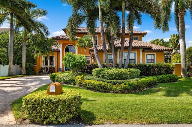 mediterranean / spanish house featuring a tiled roof, decorative driveway, a front yard, and fence