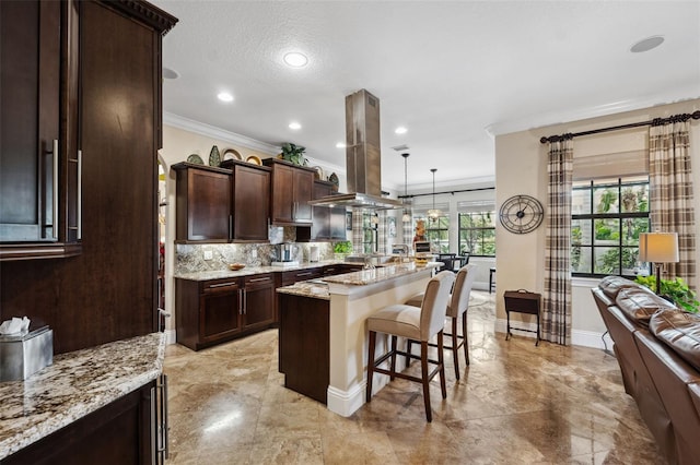 kitchen with island exhaust hood, a breakfast bar area, backsplash, ornamental molding, and dark brown cabinetry