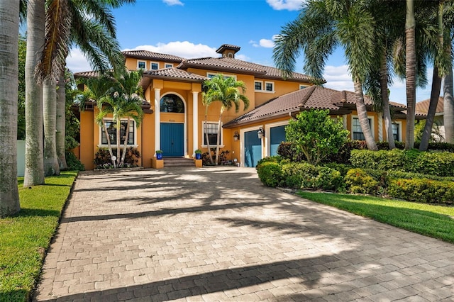 mediterranean / spanish home with a garage, a tiled roof, stucco siding, and decorative driveway