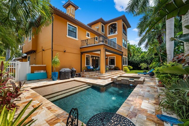 back of property with an outdoor pool, a balcony, stucco siding, a patio area, and an in ground hot tub