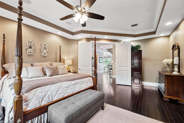 bedroom with a tray ceiling, wood finished floors, visible vents, and crown molding