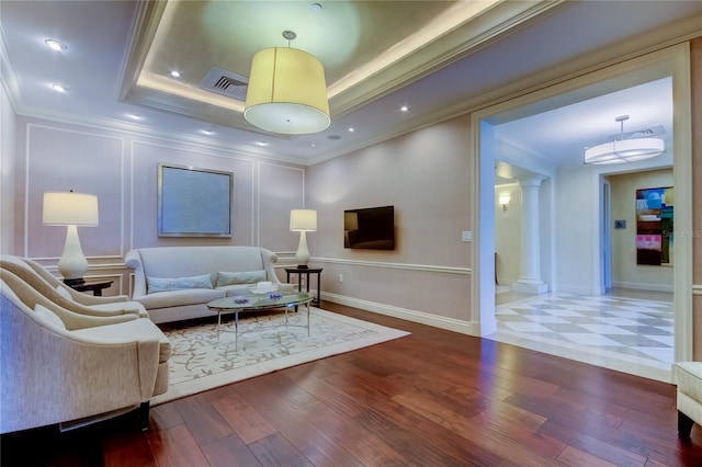 living room with crown molding, wood-type flooring, a tray ceiling, and ornate columns