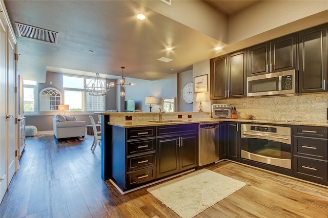 kitchen featuring appliances with stainless steel finishes, decorative light fixtures, kitchen peninsula, and sink