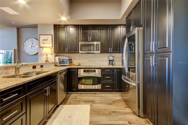 kitchen with sink, light stone counters, tasteful backsplash, light wood-type flooring, and stainless steel appliances