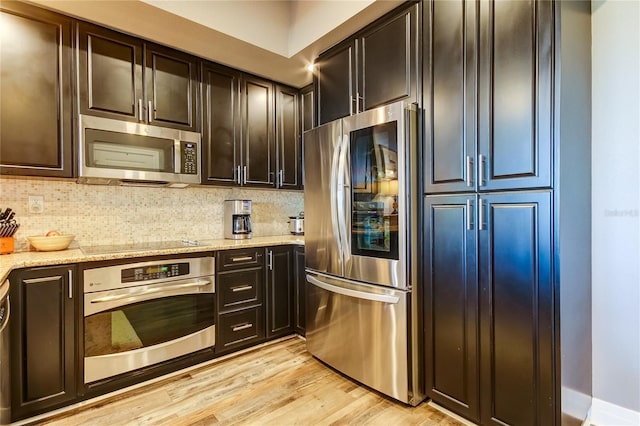 kitchen with dark brown cabinetry, light stone counters, appliances with stainless steel finishes, light hardwood / wood-style floors, and backsplash