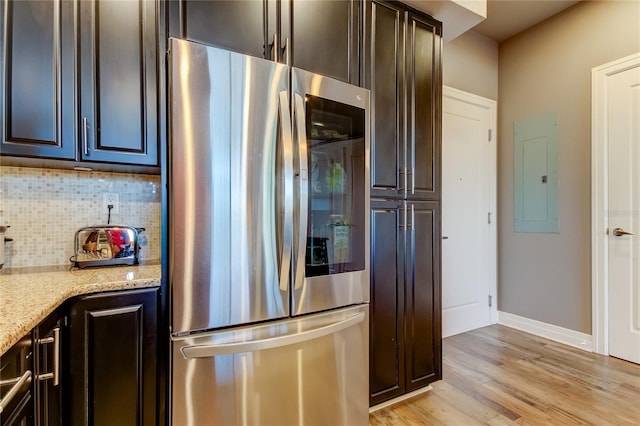 kitchen with stainless steel fridge, backsplash, electric panel, dark brown cabinetry, and light stone countertops