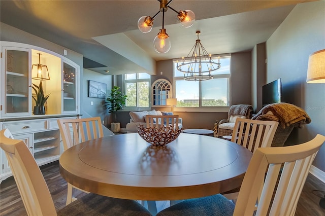 dining area with a notable chandelier, dark wood-type flooring, and a raised ceiling