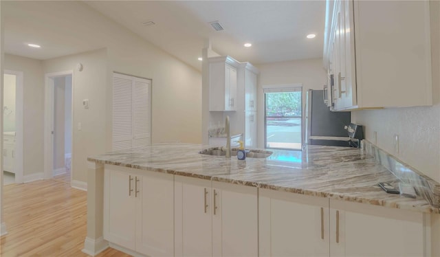 kitchen with light wood-type flooring, white cabinets, kitchen peninsula, and light stone countertops