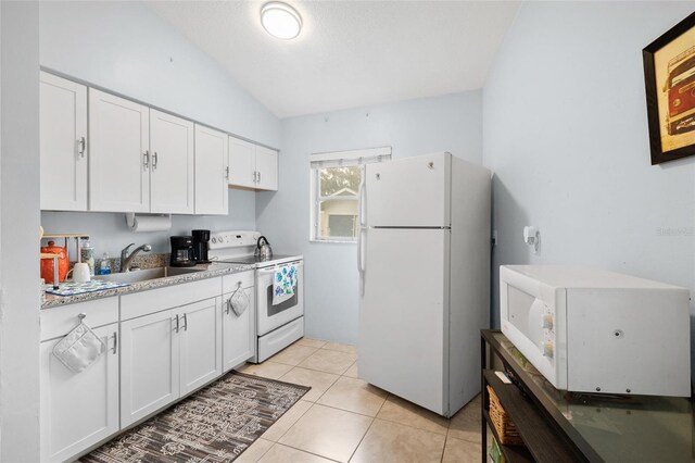 kitchen with lofted ceiling, white appliances, sink, light tile patterned floors, and white cabinetry