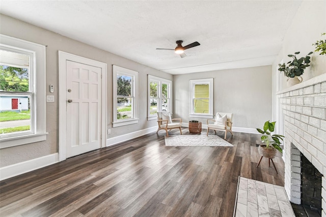 sitting room with ceiling fan, a healthy amount of sunlight, dark hardwood / wood-style floors, and a brick fireplace