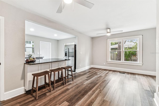 interior space with stainless steel fridge with ice dispenser, kitchen peninsula, dark wood-type flooring, and a kitchen breakfast bar