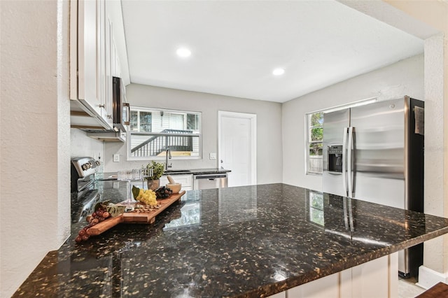 kitchen with appliances with stainless steel finishes, white cabinetry, sink, kitchen peninsula, and dark stone counters