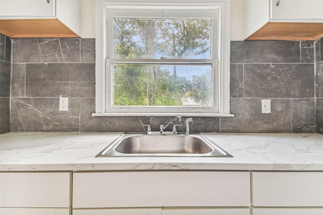 kitchen with light stone countertops, sink, white cabinetry, and backsplash