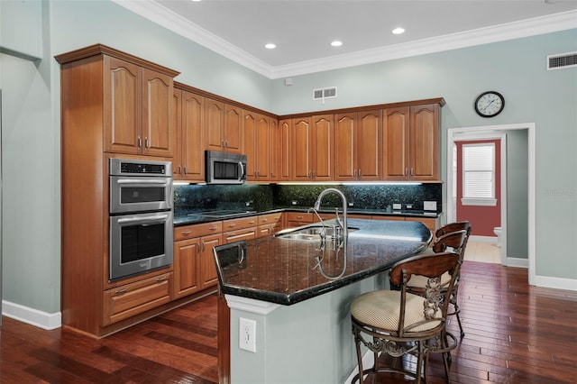 kitchen with stainless steel appliances, a center island with sink, sink, and ornamental molding