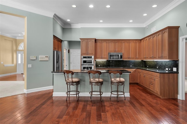 kitchen with appliances with stainless steel finishes, crown molding, a kitchen island with sink, and decorative backsplash