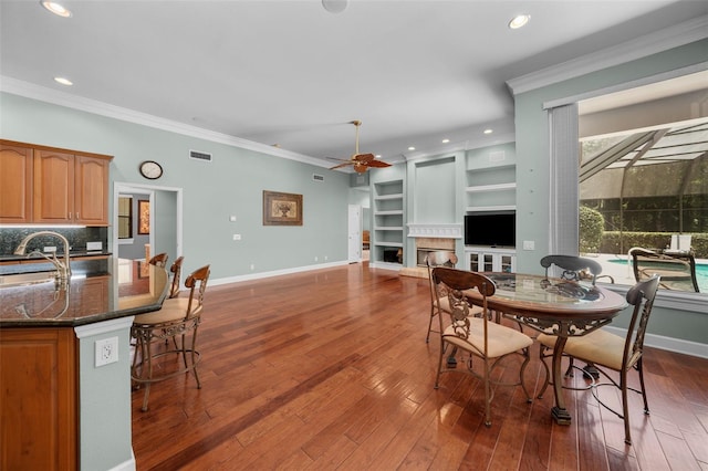 dining area featuring sink, dark wood-type flooring, built in features, and crown molding