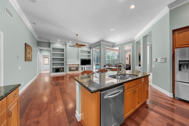 kitchen featuring an island with sink, appliances with stainless steel finishes, built in features, dark stone countertops, and sink