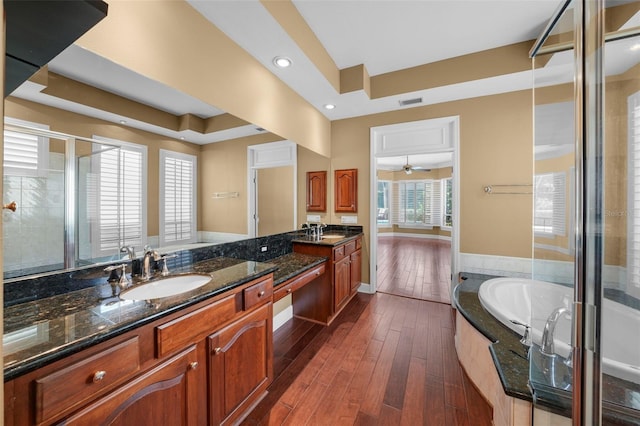 bathroom featuring ceiling fan, hardwood / wood-style flooring, vanity, a tray ceiling, and plus walk in shower