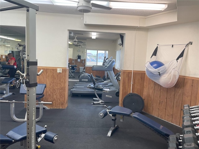 gym with a textured ceiling, ceiling fan, and wood walls