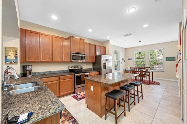 kitchen with a breakfast bar area, a sink, appliances with stainless steel finishes, brown cabinets, and decorative light fixtures