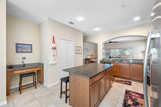 kitchen featuring ceiling fan, sink, a center island, and dark stone counters