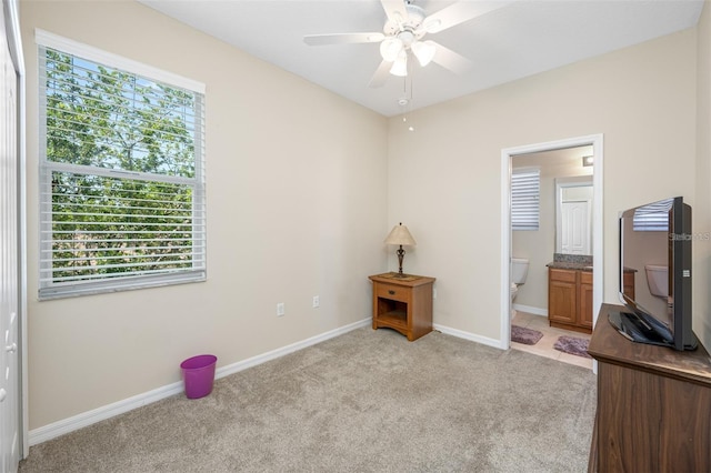 unfurnished bedroom with baseboards, ensuite bath, a ceiling fan, and light colored carpet