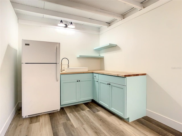 kitchen featuring sink, beamed ceiling, white refrigerator, butcher block countertops, and light hardwood / wood-style floors