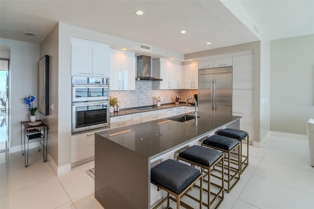 kitchen featuring stainless steel appliances, a center island with sink, a breakfast bar, and wall chimney range hood