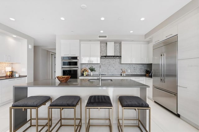 kitchen with stainless steel appliances, visible vents, white cabinetry, a sink, and wall chimney range hood