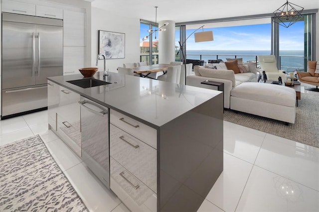 kitchen with stainless steel appliances, a water view, hanging light fixtures, a sink, and a large island with sink