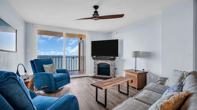 living room with ceiling fan, light wood-type flooring, expansive windows, and a fireplace