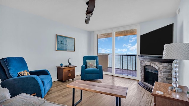 living room featuring ceiling fan, light hardwood / wood-style flooring, and a stone fireplace