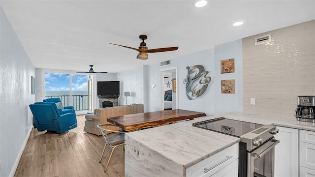 kitchen with ceiling fan, a fireplace, white cabinets, and electric range