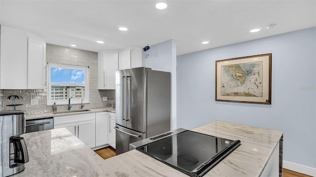 kitchen with stainless steel appliances, backsplash, light stone countertops, white cabinets, and sink