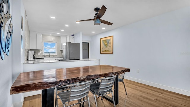 kitchen with kitchen peninsula, stainless steel fridge, ceiling fan, decorative backsplash, and white cabinets