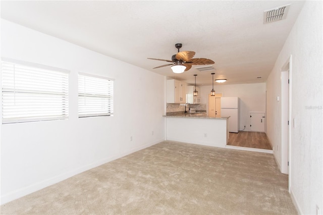 unfurnished living room with light colored carpet, ceiling fan, and sink