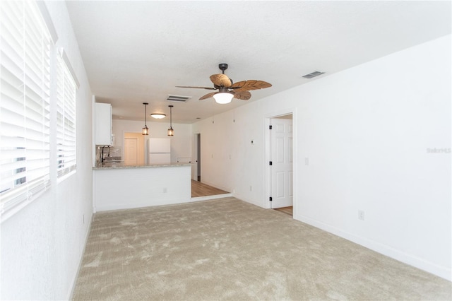 unfurnished living room with light colored carpet and ceiling fan