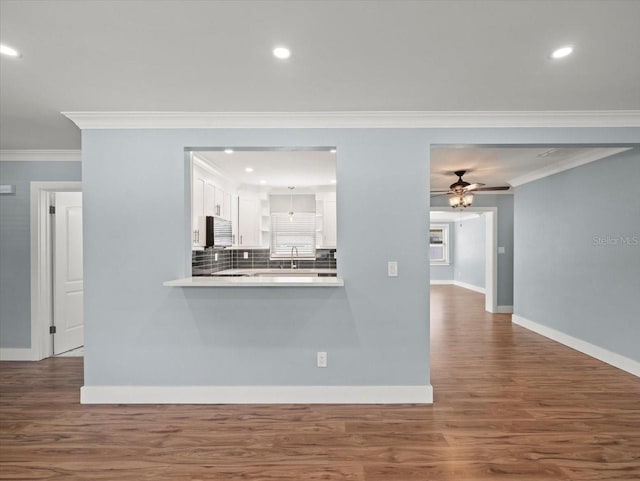 unfurnished living room featuring sink, wood-type flooring, ornamental molding, and ceiling fan