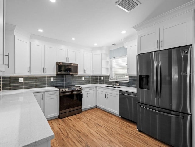 kitchen featuring appliances with stainless steel finishes, decorative light fixtures, white cabinets, backsplash, and light hardwood / wood-style floors