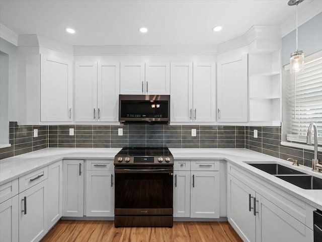 kitchen with appliances with stainless steel finishes, white cabinetry, sink, decorative backsplash, and light hardwood / wood-style flooring