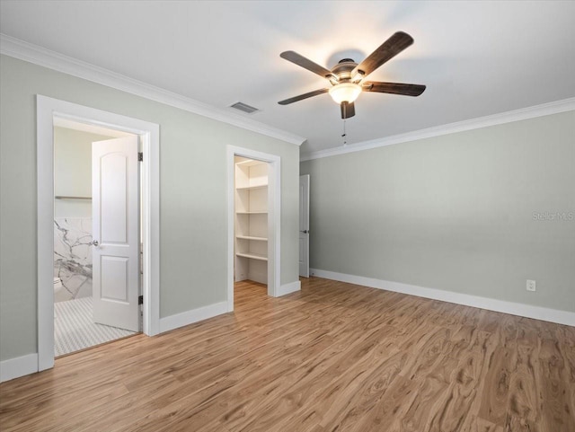 unfurnished bedroom featuring ornamental molding, a spacious closet, a closet, and light wood-type flooring