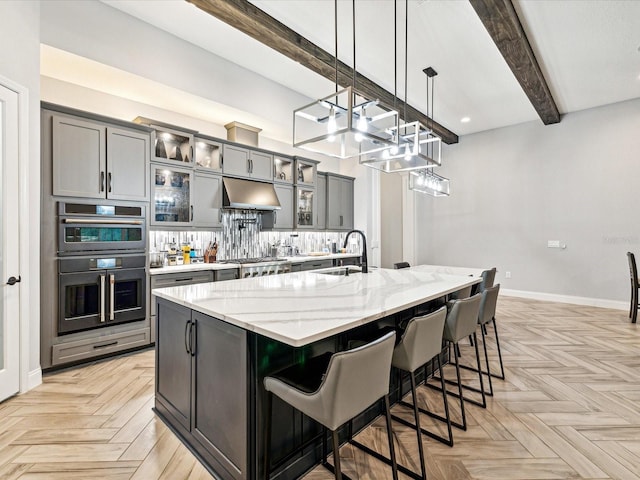 kitchen with light stone countertops, hanging light fixtures, beamed ceiling, a spacious island, and a breakfast bar area