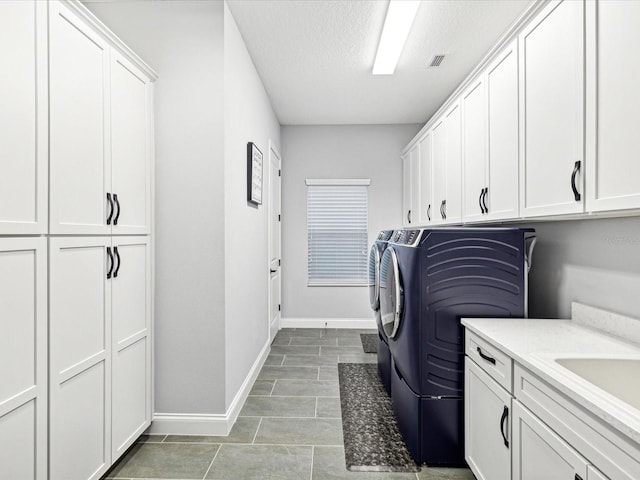 clothes washing area with cabinets, a textured ceiling, sink, washer and dryer, and light tile patterned flooring