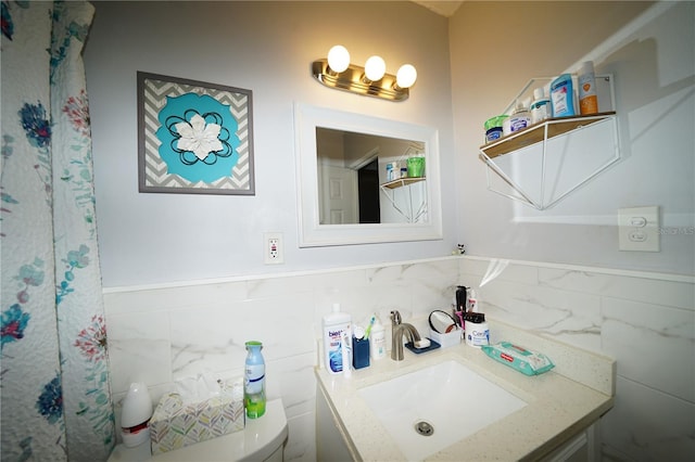 bathroom with tile walls, a wainscoted wall, vanity, and toilet