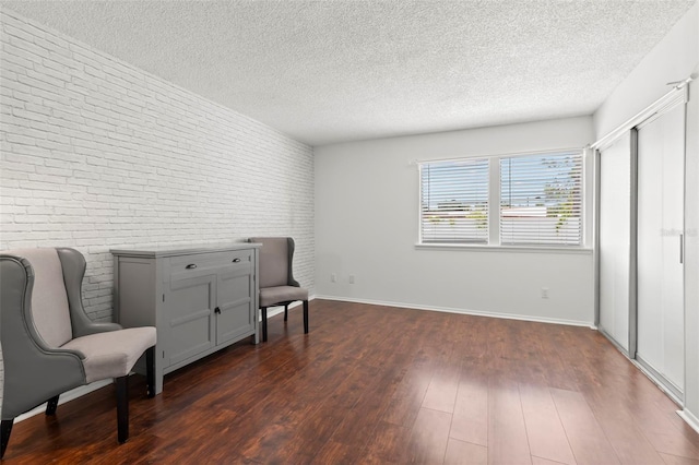 living area featuring dark hardwood / wood-style floors, a textured ceiling, and brick wall