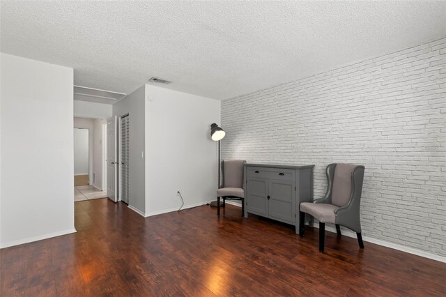 sitting room featuring a textured ceiling, brick wall, and dark hardwood / wood-style floors