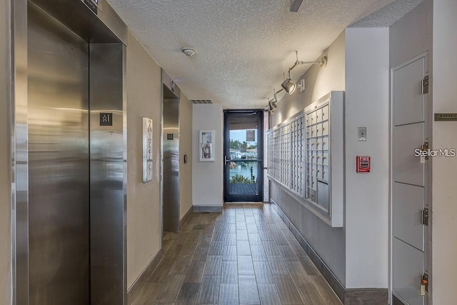 hallway featuring a textured ceiling, elevator, dark hardwood / wood-style flooring, and a mail area